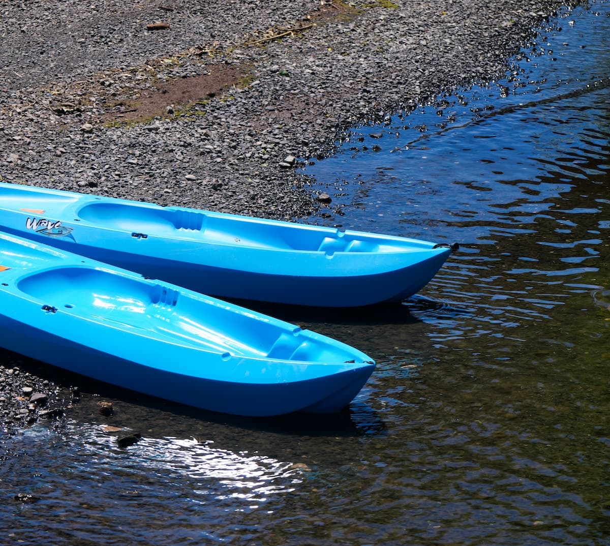 Two blue kayaks pulled up on the gravel shoreline