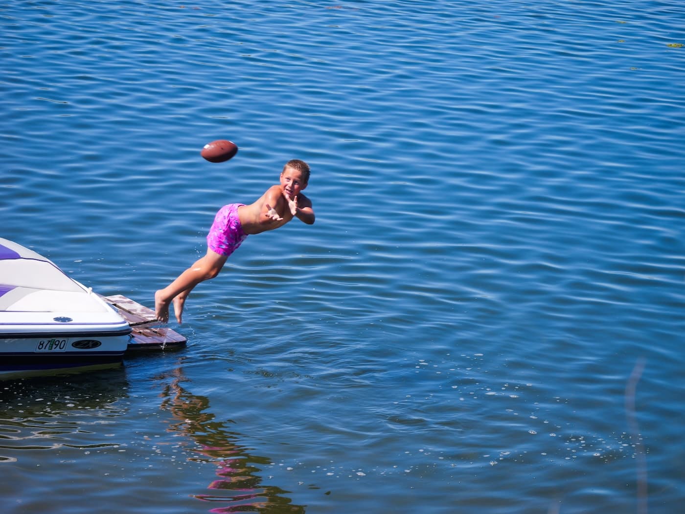 A girl launching off a swim platform after a football