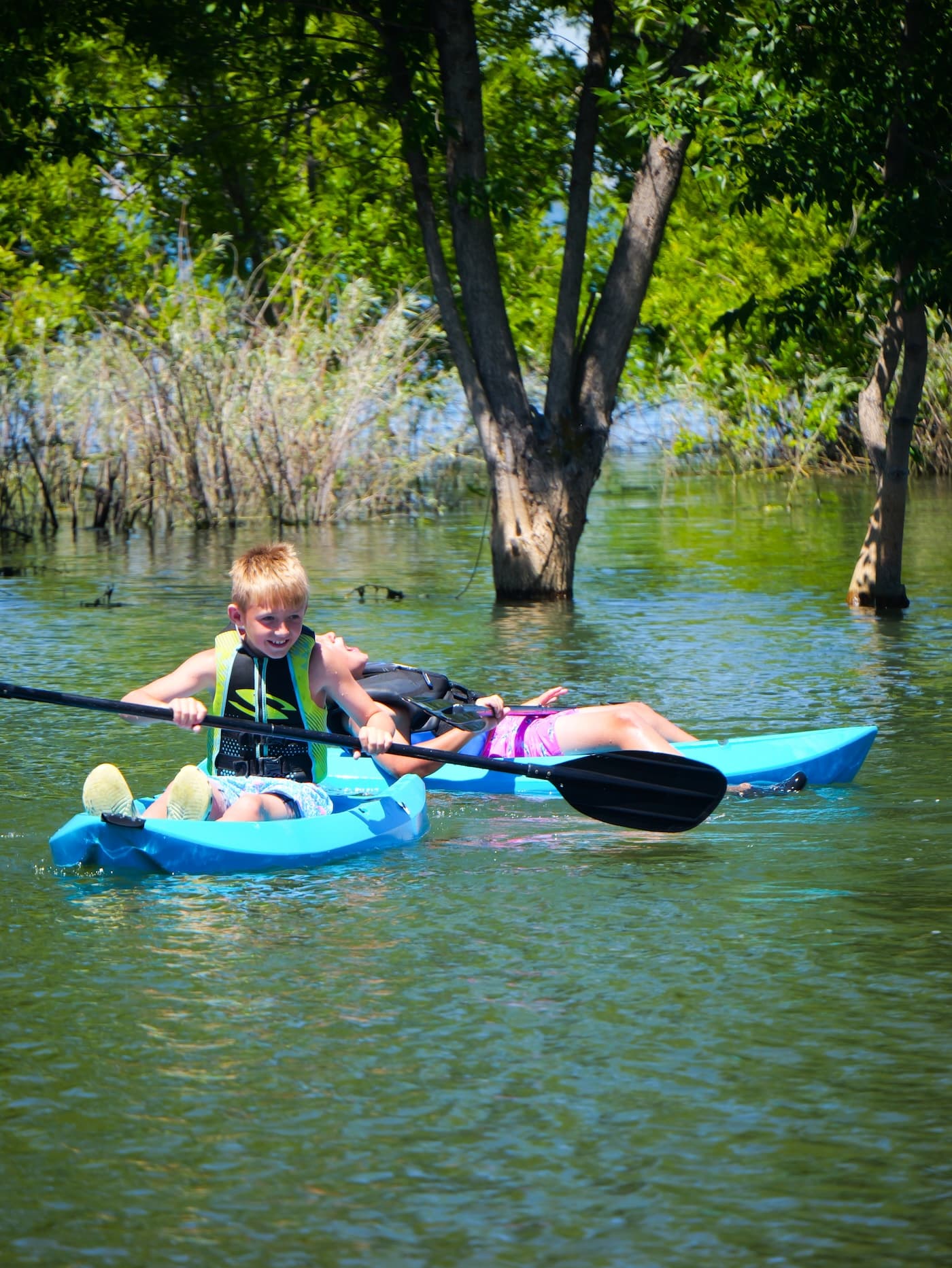 Two children paddling kayaks through the flooded timber