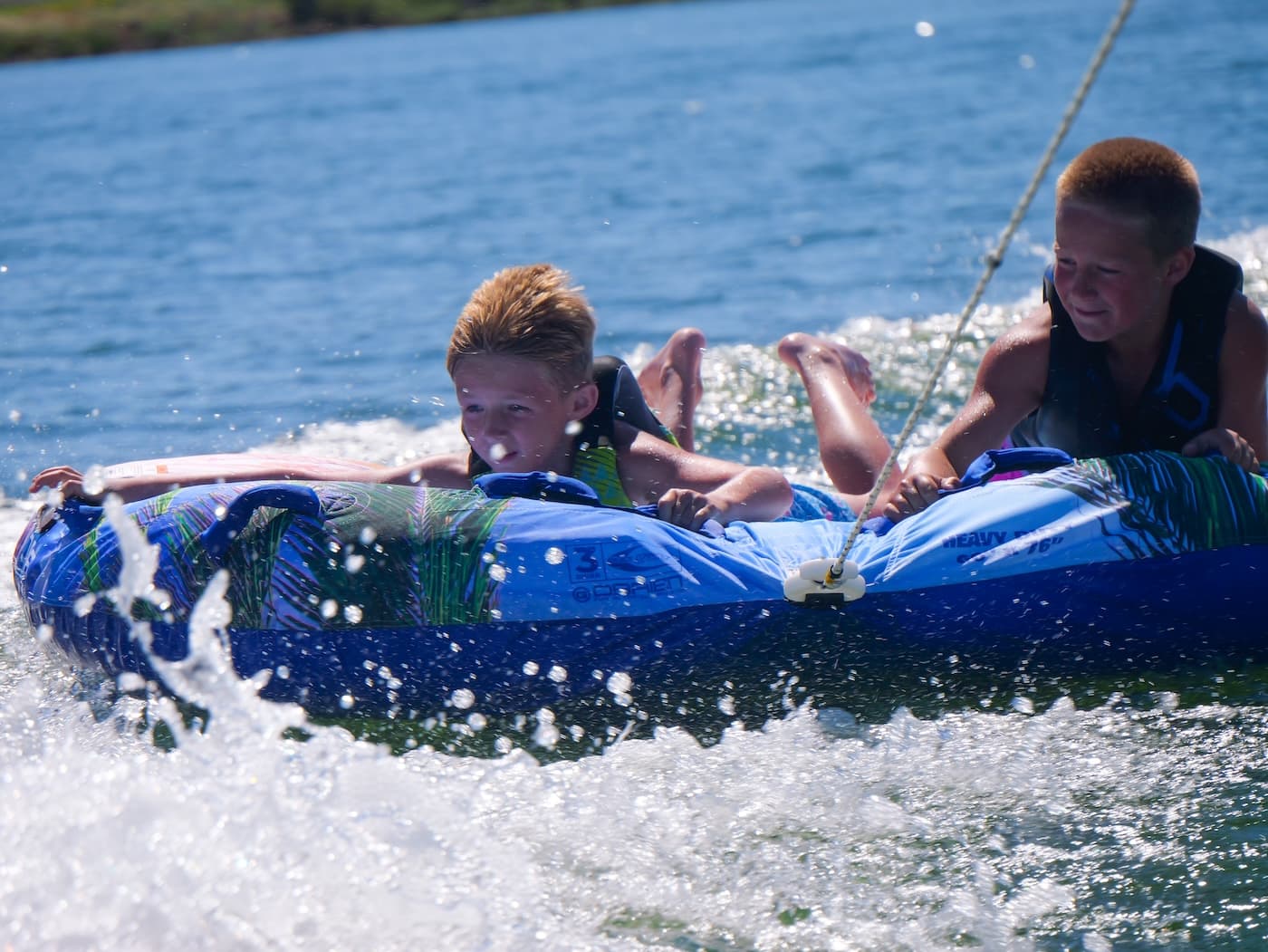 Two kids hanging onto a tube through the spray behind a boat