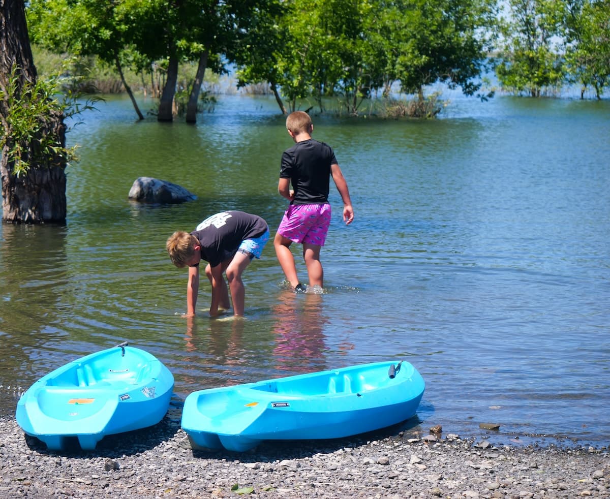 Two kids wading in the shallows beside their beached kayaks