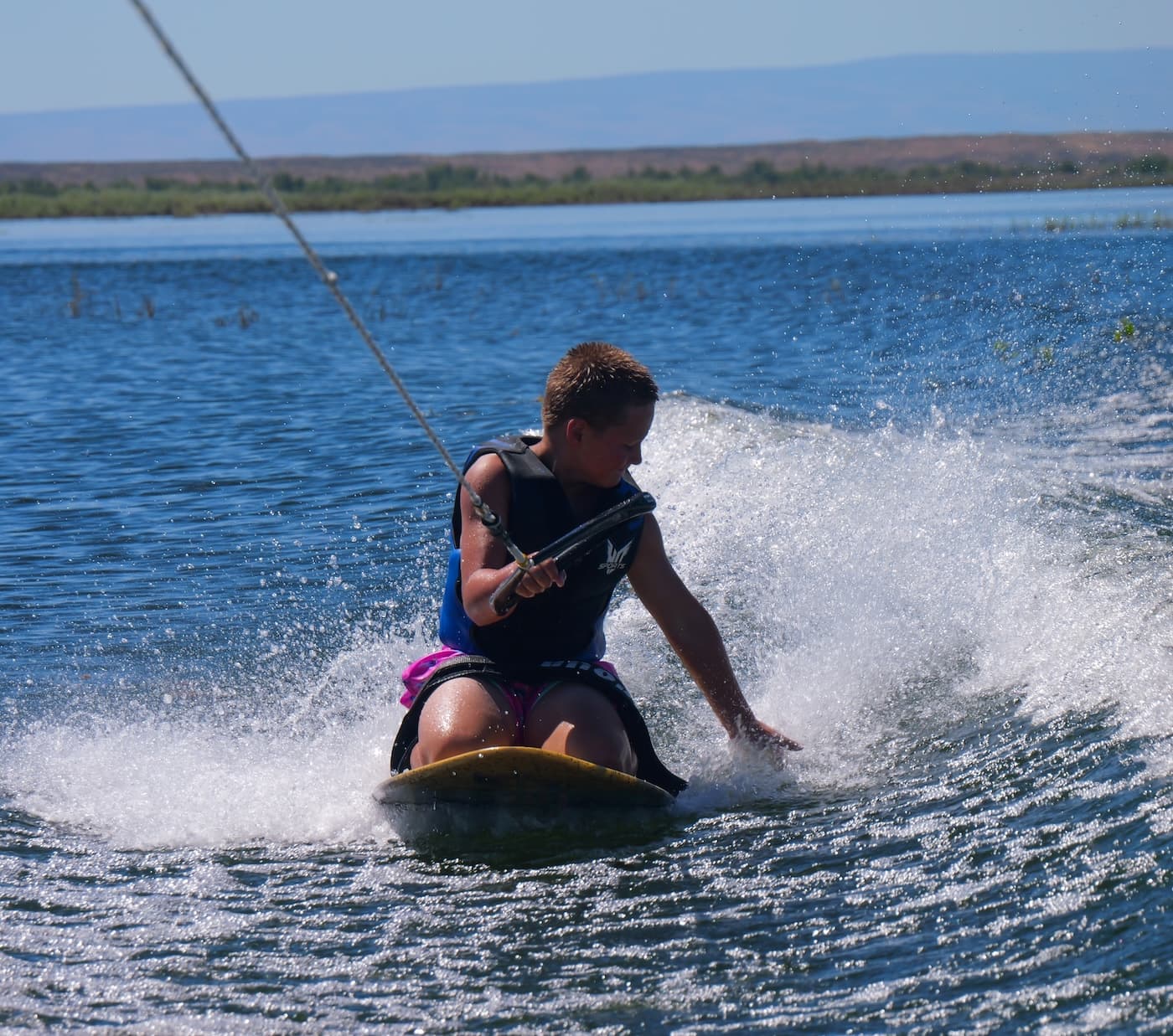 A kid carving across the wake on a kneeboard behind a boat
