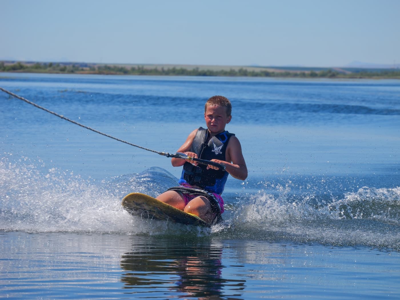 A kid kneeboarding across open water on a blue sky day