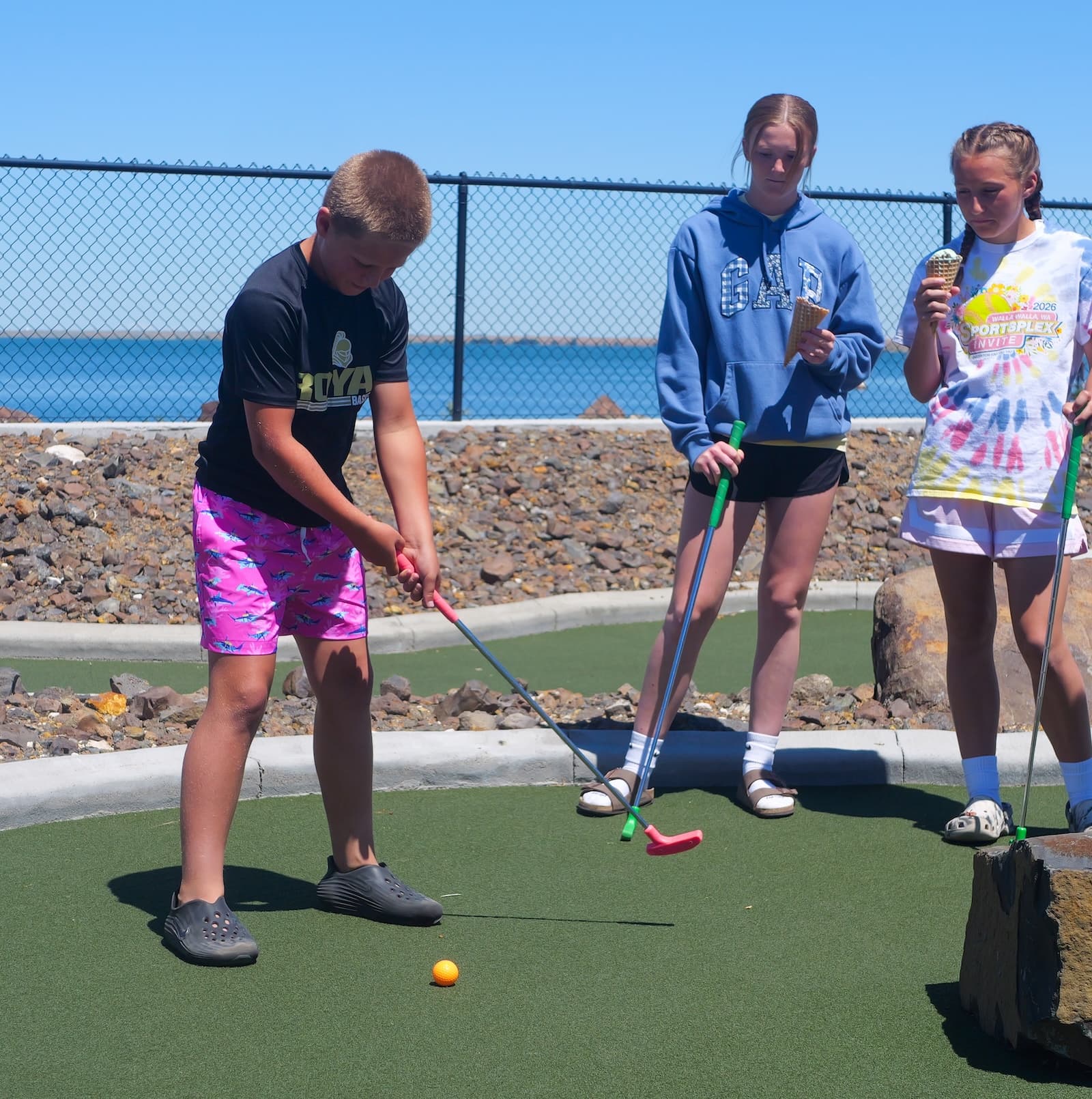 A player putting on a green edged with concrete curbing and rock beds, the reservoir behind